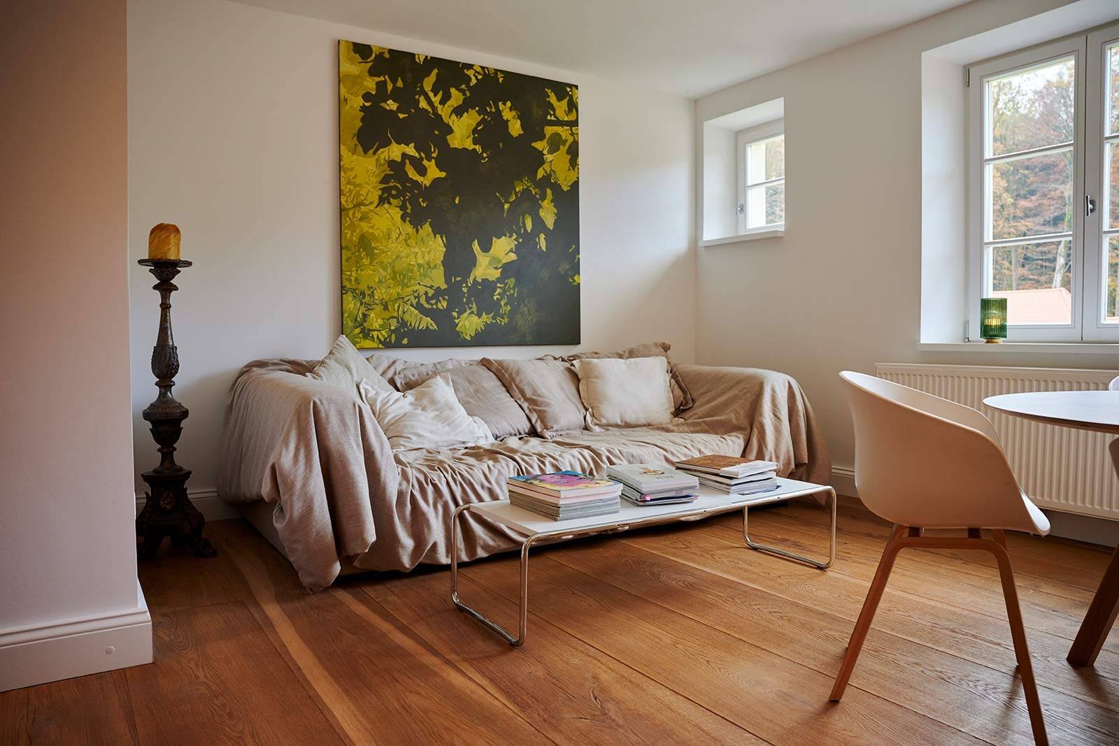 Wohnbereich mit Sofa, großformatigem gelbem Kunstwerk und Holzdielen