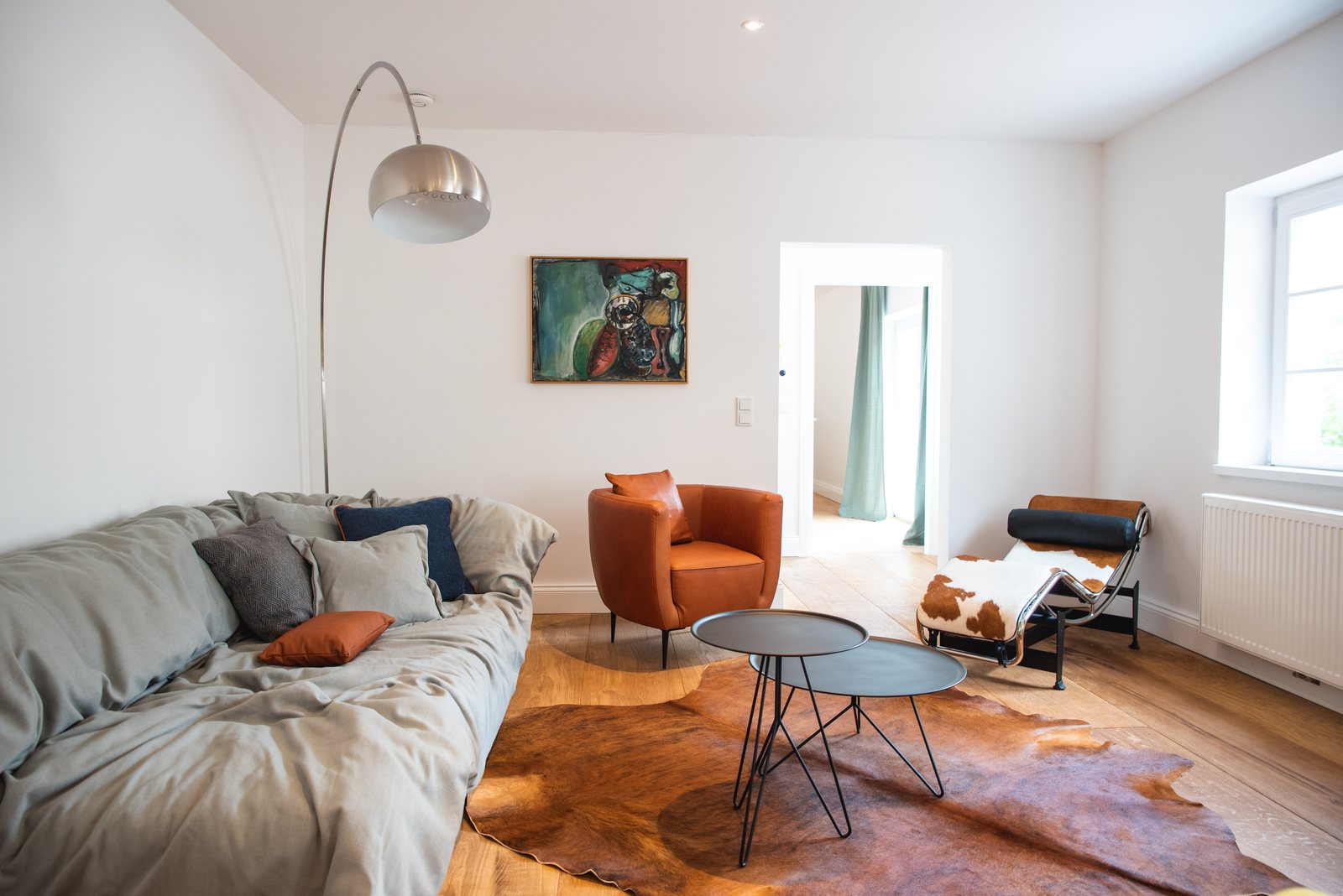 Wohnzimmer mit Sofa, Kuhfell und orangefarbenem Sessel